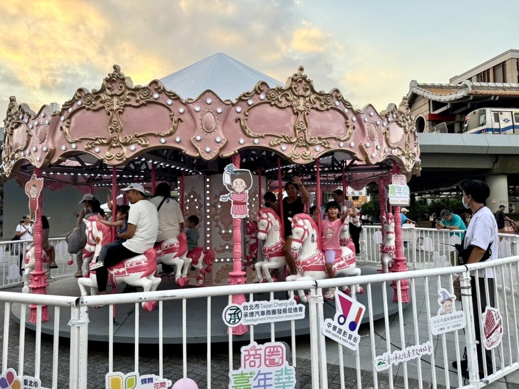 爸爸媽媽帶著小朋友一起享受商圈嘉年華活動現場的旋轉木馬。（圖/臺北市商業處提供）