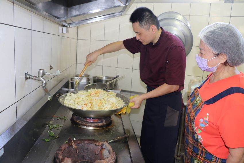 惜食分享廚房開伙 五星級主廚陳佳瑋為長輩掌廚 7 《圖說》五星級飯店主廚的陳佳瑋專程到新莊牡丹心社區發展協會照顧關懷據點為長輩義煮,志工在一旁討教。〈社會局提供〉